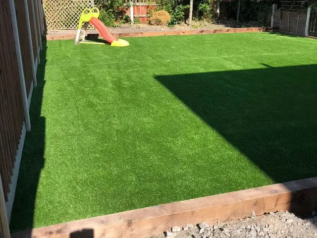 The finished artificial lawn edged with timber sleepers, with a child's slide at the far end