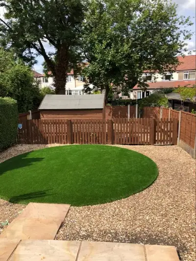 Circular artificial lawn set into a gravel garden, with stone paving in front and a timber fence behind