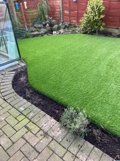 Curved artificial lawn beside a conservatory, edged by a block-paved path and a planted border