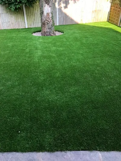 Artificial lawn fitted neatly around the trunk of a mature tree, against a pale fence