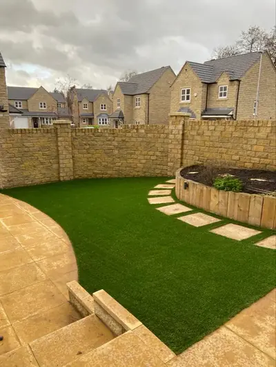 Curved artificial lawn below a sandstone garden wall, with stepping stones set into the grass