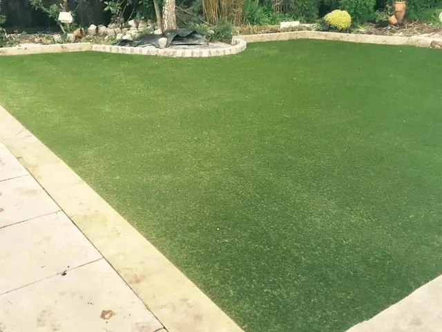 The same garden with a smooth artificial lawn framed by a pale stone patio and a curved border
