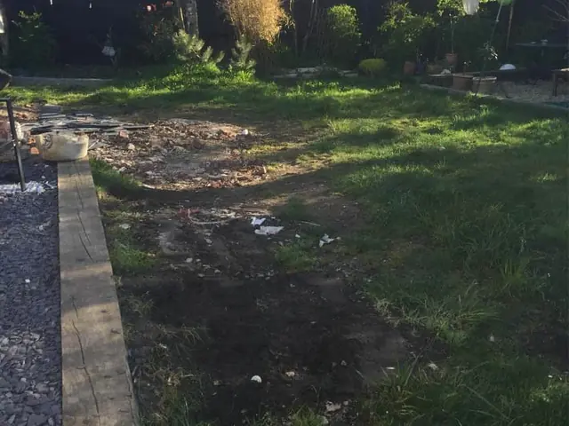 Garden before the work: patchy grass and bare earth beside a timber sleeper edge