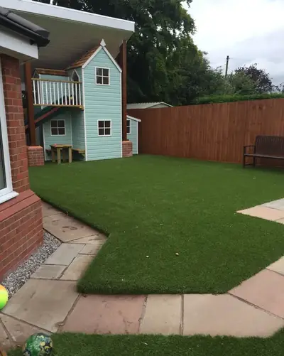 Artificial lawn with stone paving in a family garden, in front of a pale blue two-storey wendy house
