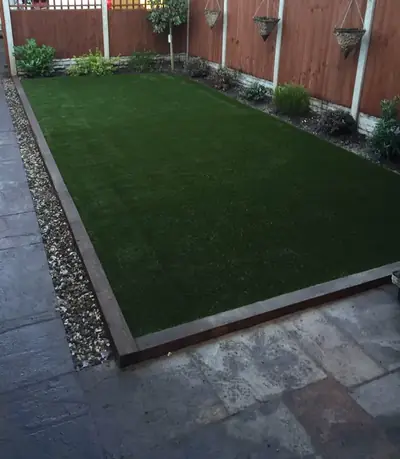 Rectangular artificial lawn edged with timber sleepers and a strip of pebbles, inside a grey stone patio